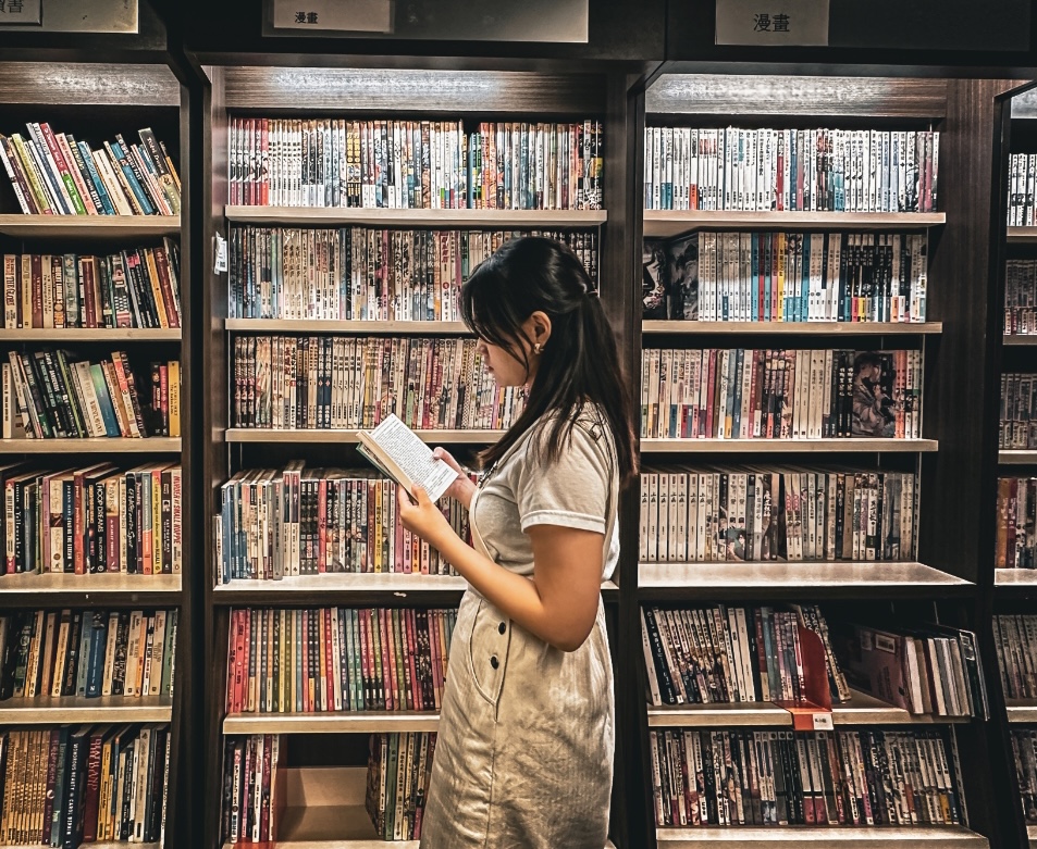 Girl in white overall dress reading a book at the manga section.